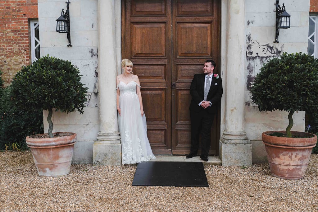 Bride & Groom leaning on the pillars of the doorway at the main house at Braxted Park wedding venue