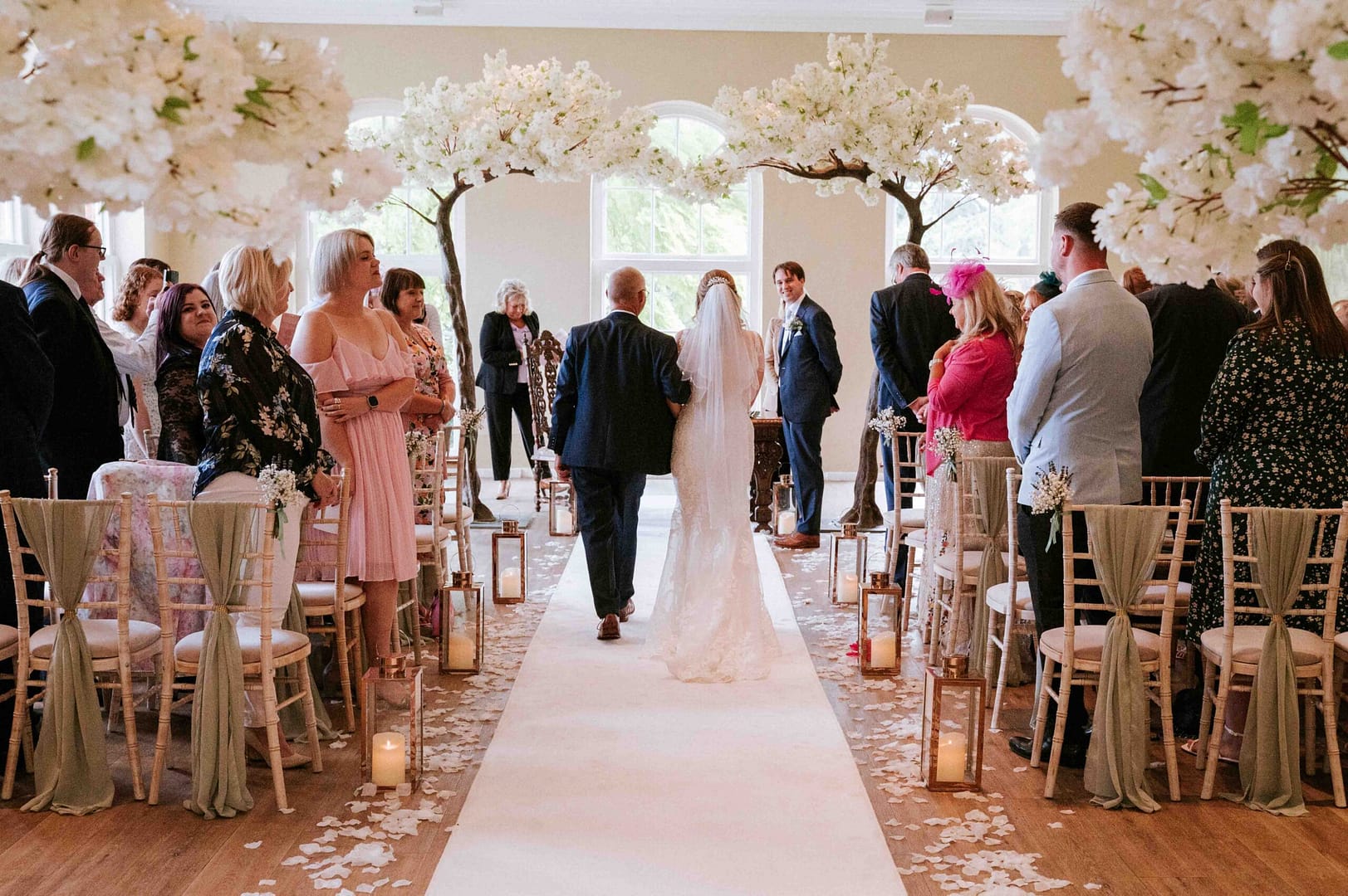 Catherine Brooks Photography - A wedding ceremony taking place in a room filled with whit blossom trees