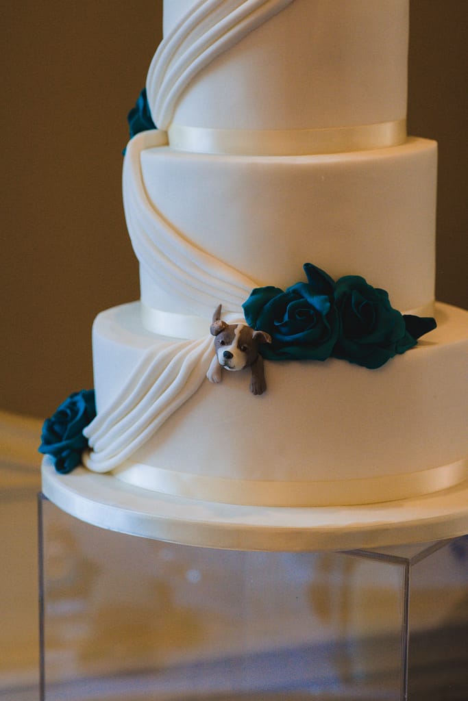 Small dog made of icing escaping out of a white wedding cake.